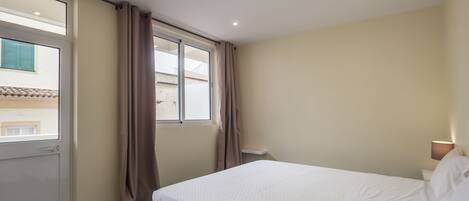 A hotel room with a bed, a window with curtains, a door, and a ceiling light.