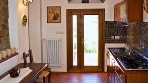Une cuisine avec un mur recouvert de carreaux, des armoires en bois, une cuisinière et un coin repas comprenant une table et des chaises.