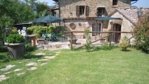 Un bâtiment en pierre avec un escalier en pierre menant à une porte. On y trouve des plantes en pot et une table avec des chaises à l’extérieur.