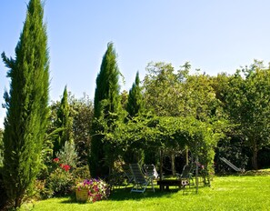 Un jardin agrémenté d’une pergola, d’un espace salon extérieur et d’une variété d’arbres et d’arbustes.