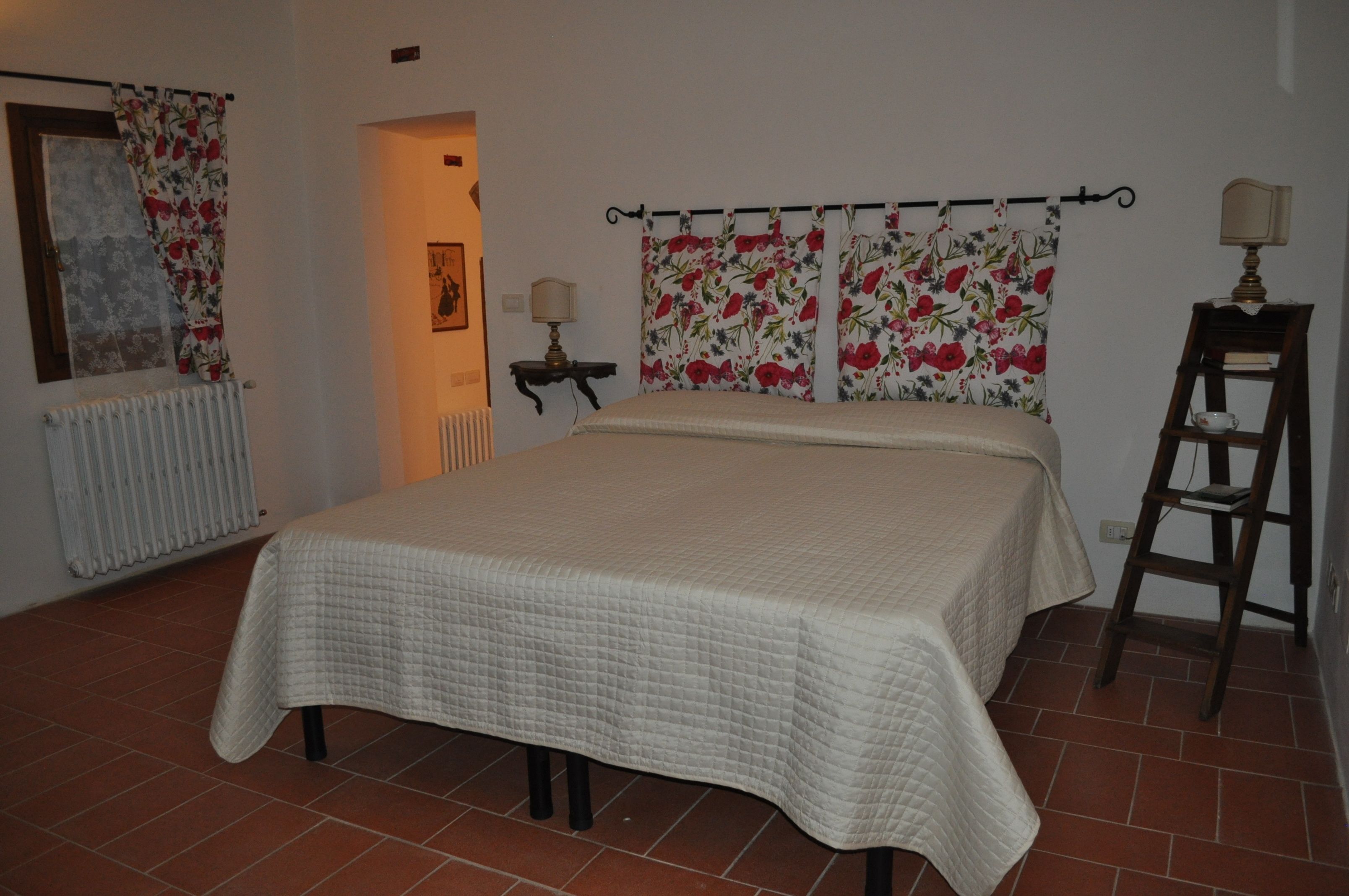 A bedroom with a bed, a radiator, a lamp, a chair, and a window with curtains.
