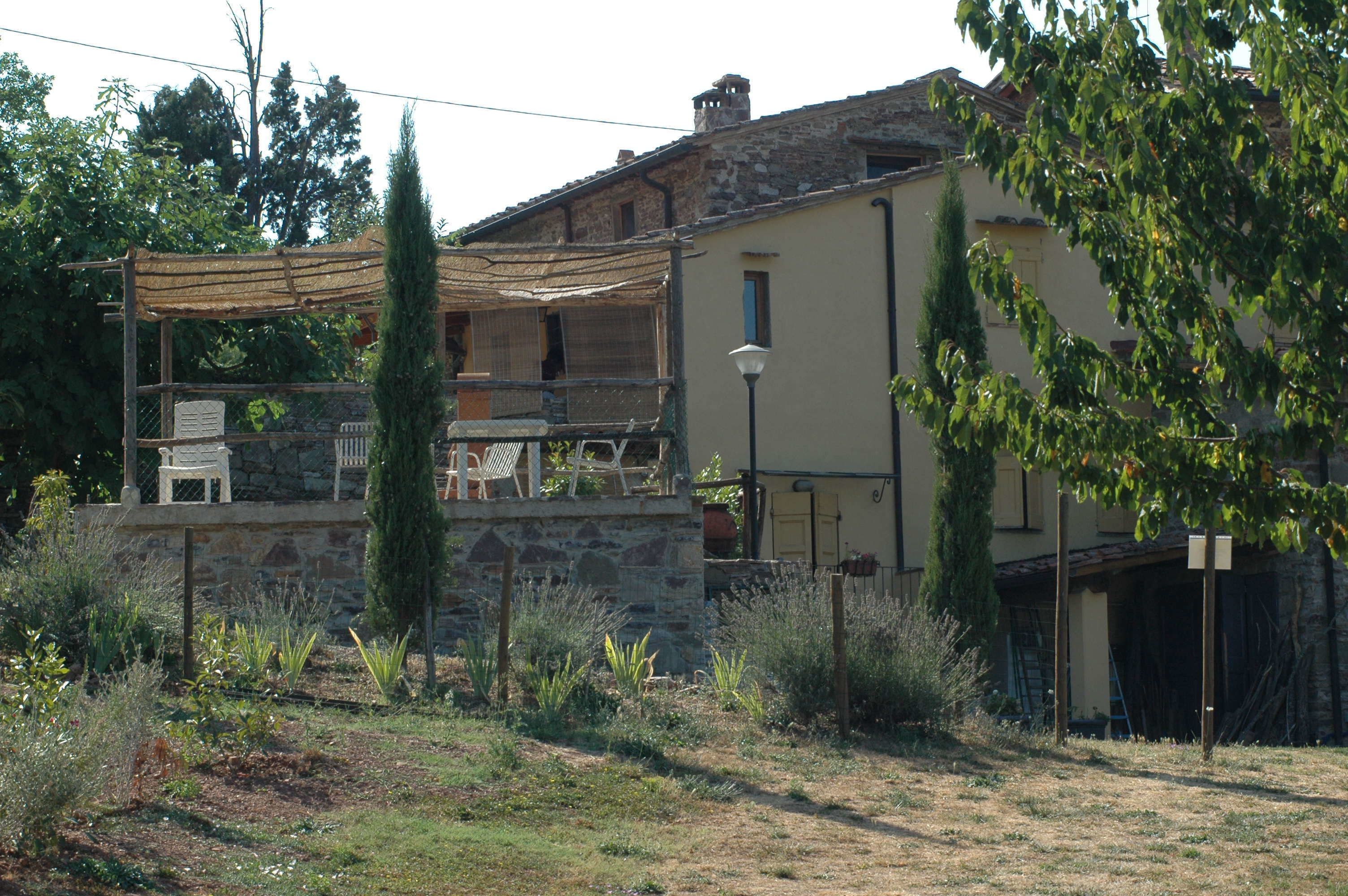 A rustic house with a stone wall, a wooden pergola, and a garden with various plants.