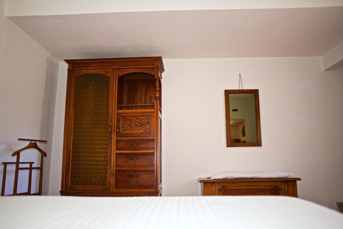 A bedroom with a large wooden wardrobe, a bed with a white bedspread, and a mirror on the wall.