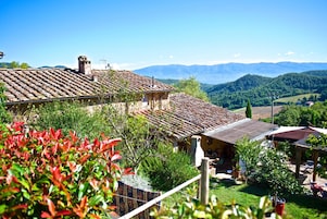 A rustic building with a tiled roof, surrounded by greenery and mountains in the background.