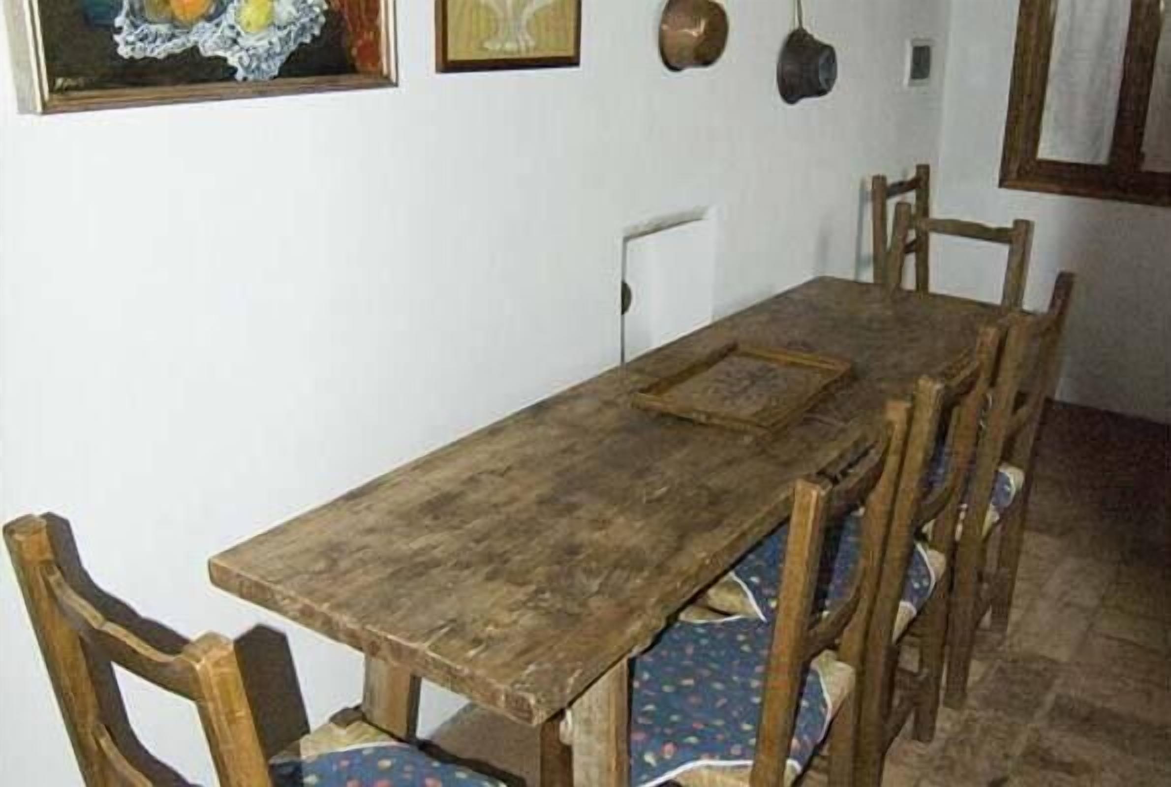 Un comedor con una mesa y sillas de madera, un cuadro en la pared y una ventana con cortinas.