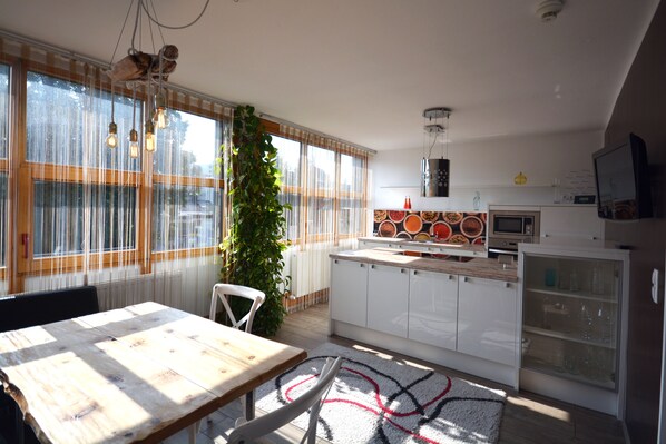 Una cocina moderna con armarios blancos, una mesa de madera y un ventanal con cortinas.