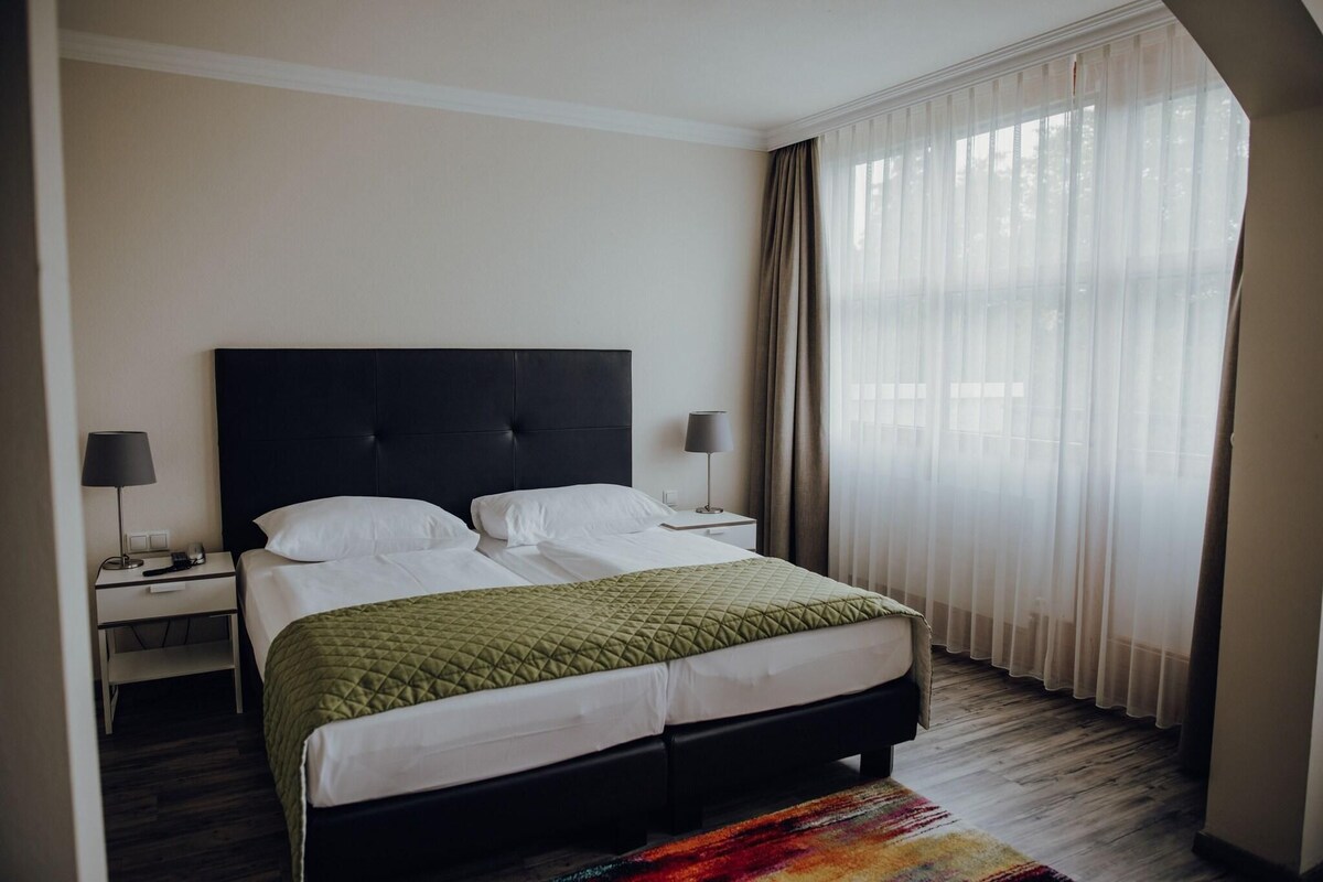 Una habitación de hotel con cama, mesitas de noche y una ventana con cortinas.
