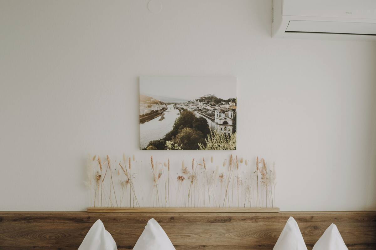 Habitación de hotel con dos camas, cabecera de madera, aire acondicionado de pared, un cuadro enmarcado y plantas secas en un estante.