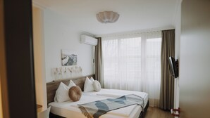 Una cama bien hecha con una manta, una mesita de noche, un aire acondicionado instalado en la pared y una ventana con cortinas.