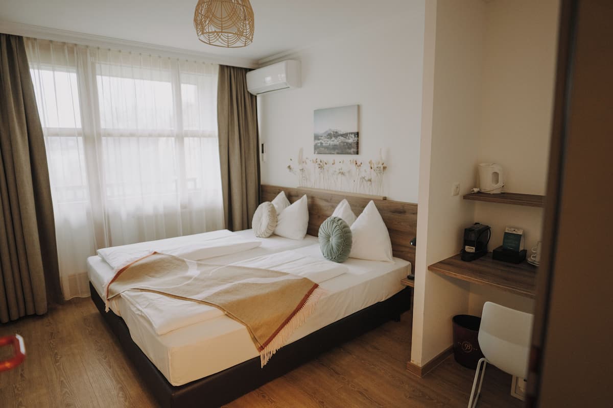 Una cama bien hecha con cabecera de madera, una mesita de noche con cafetera y aire acondicionado instalado en la pared.