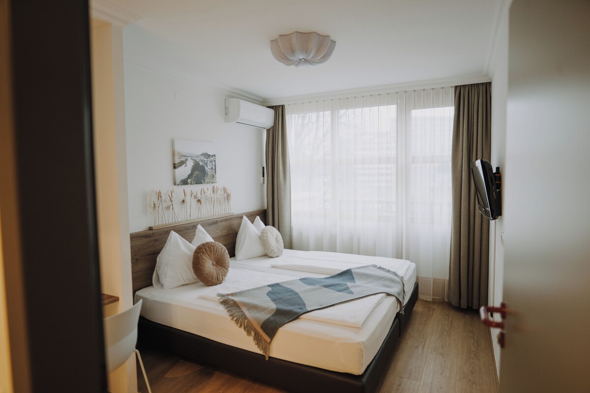 Un dormitorio ordenado con cama, mesita de noche, aire acondicionado instalado en la pared y ventana con cortinas.