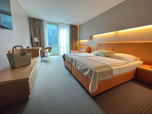 A hotel room with a bed, bedside tables, a desk, a chair, and a view of the outdoors. - Thermana Park Laško (Lasko)