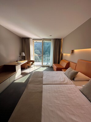 A hotel room with a bed, a desk, a chair, and a balcony with a view of the forest. - Thermana Park Laško (Lasko)