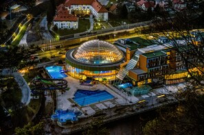 A large, circular building with a glass dome, surrounded by a swimming pool and a water slide. - Thermana Park Laško (Lasko)