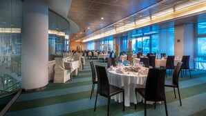 Un comedor amplio con varias mesas y sillas, ventanas grandes que ofrecen vistas al exterior y un diseño de techo moderno.