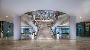 Un vestíbulo amplio con una escalera central, iluminación moderna y paredes de vidrio.