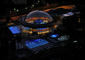 A large, circular building with a glass dome, surrounded by a swimming pool and outdoor seating areas. - Thermana Park Laško (Lasko)