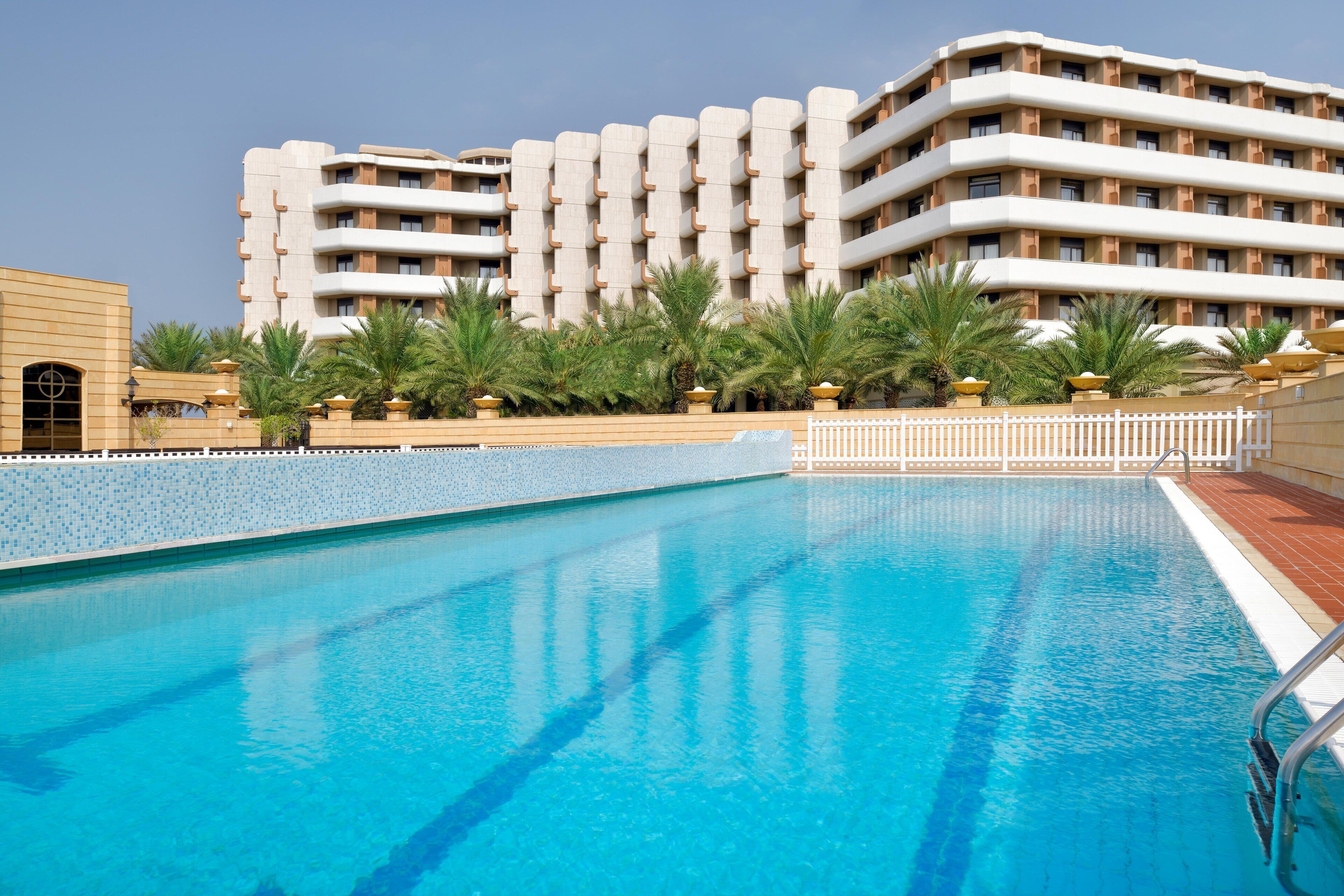 A swimming pool with a clear blue water surface, surrounded by a white fence and palm trees.