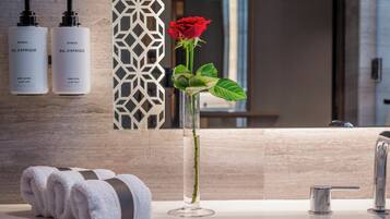 A bathroom with a white towel, a glass vase with a rose, and two bottles of BYREDO Bal d'Afrique body lotion and hand wash.