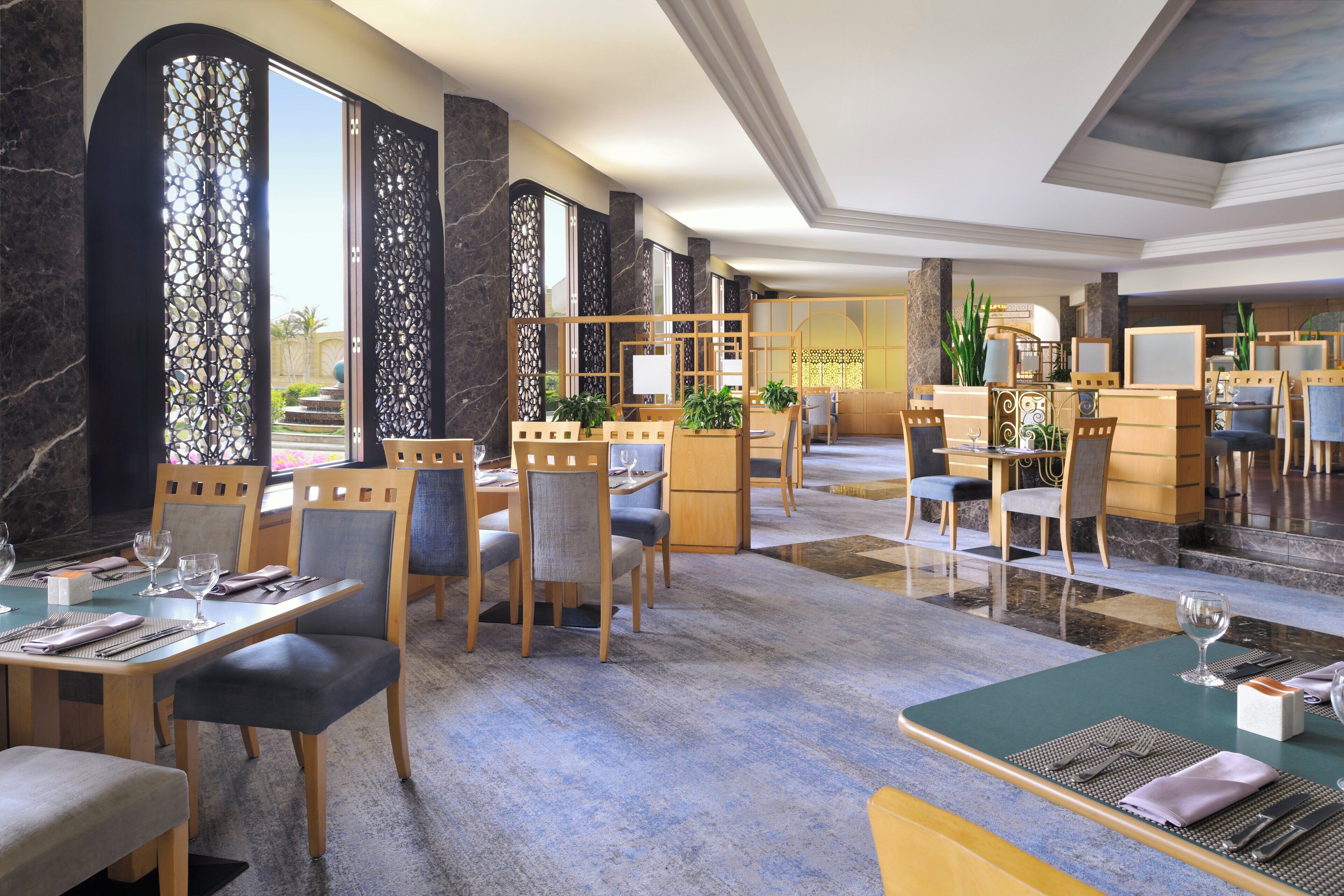 Un amplio vestíbulo de hotel con varias zonas de estar, que incluyen una recepción, mesas para comer y sillas.