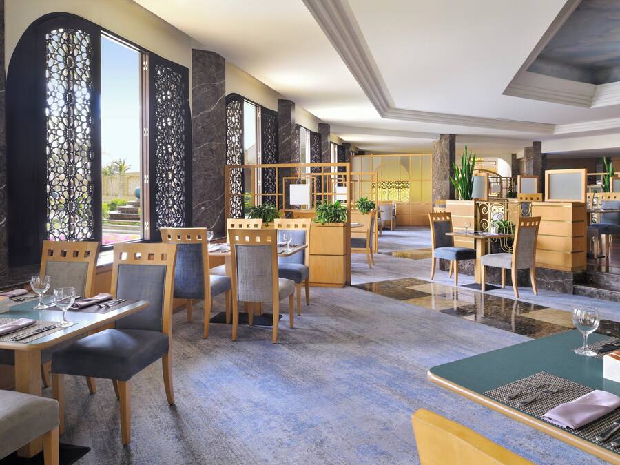 Un amplio vestíbulo de hotel con varias zonas de estar, que incluyen una recepción, mesas para comer y sillas.