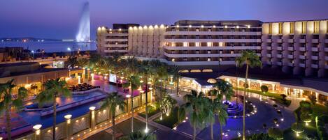 A hotel with multiple floors, a swimming pool, and a fountain.