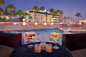 A poolside table with two cocktails and two small jars of nuts.