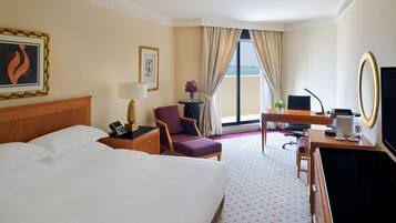 A hotel room with a large bed, a desk with a chair, a television, and a view of the beach.