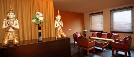 A reception desk with golden statues, a vase with white flowers, and traditional wooden furniture in a warmly lit room.