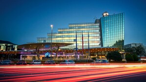A modern hotel with a distinctive curved roof and a tall, reflective glass building in the background. - Perla, Resort & Entertainment (Nova Gorica)