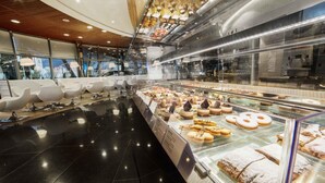A bakery display with various pastries and a seating area with white chairs. - Perla, Resort & Entertainment (Nova Gorica)