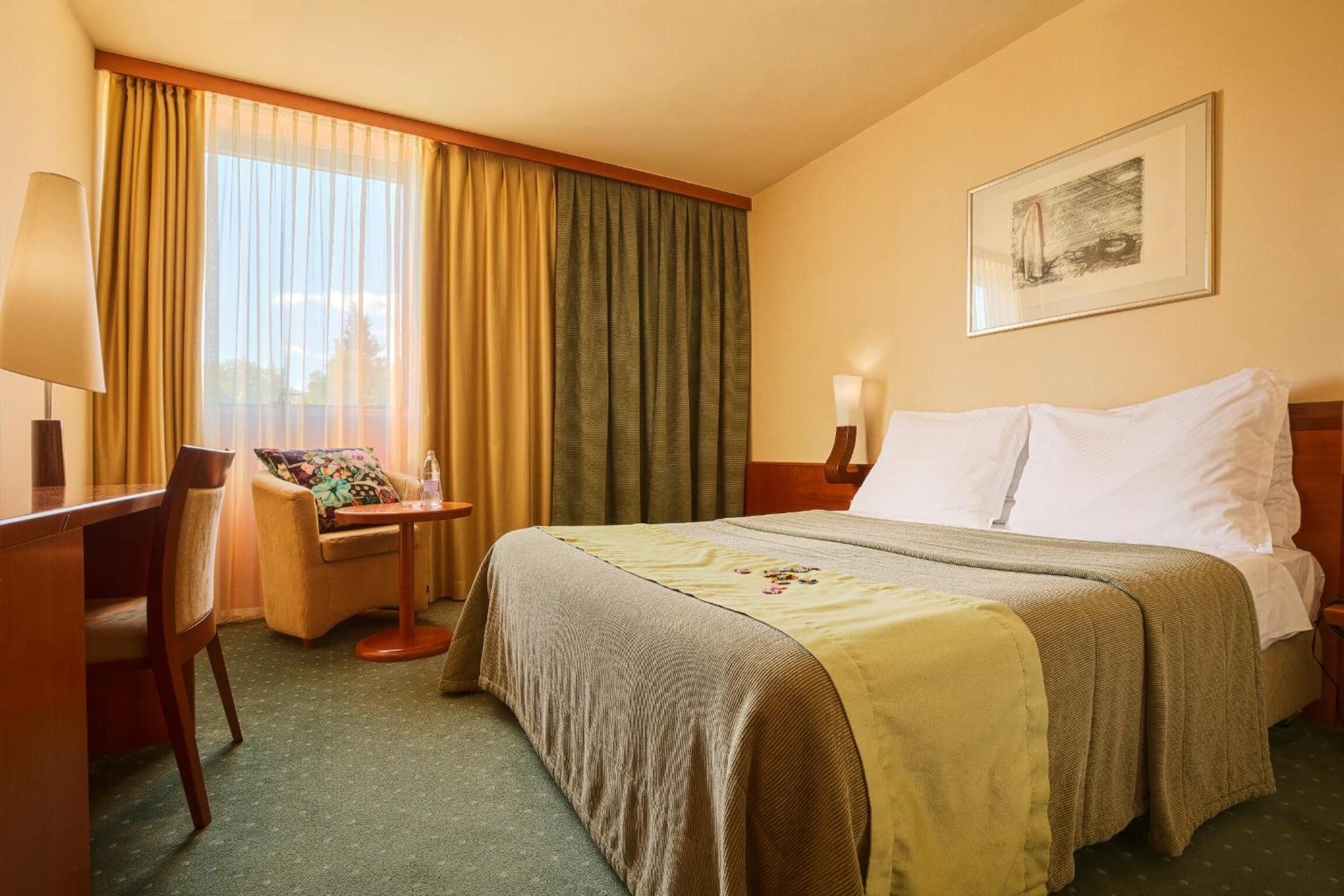 A hotel room with a bed, a desk, a chair, a lamp, and a window with curtains.