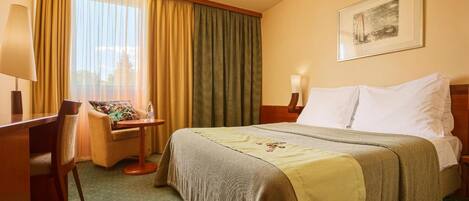 A hotel room with a bed, a desk, a chair, a lamp, and a window with curtains.