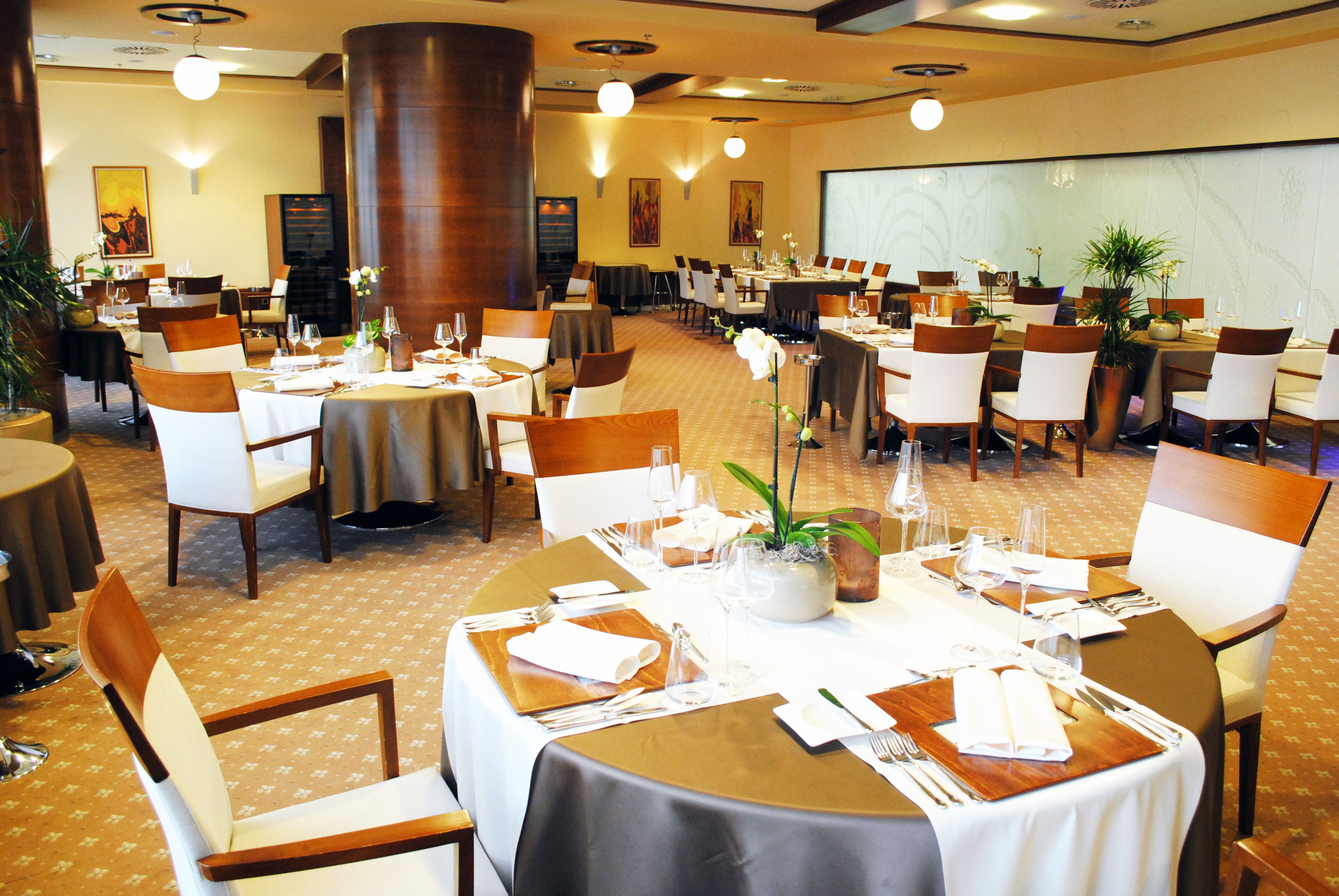 A hotel dining area with multiple tables set for dining, chairs, and potted plants.