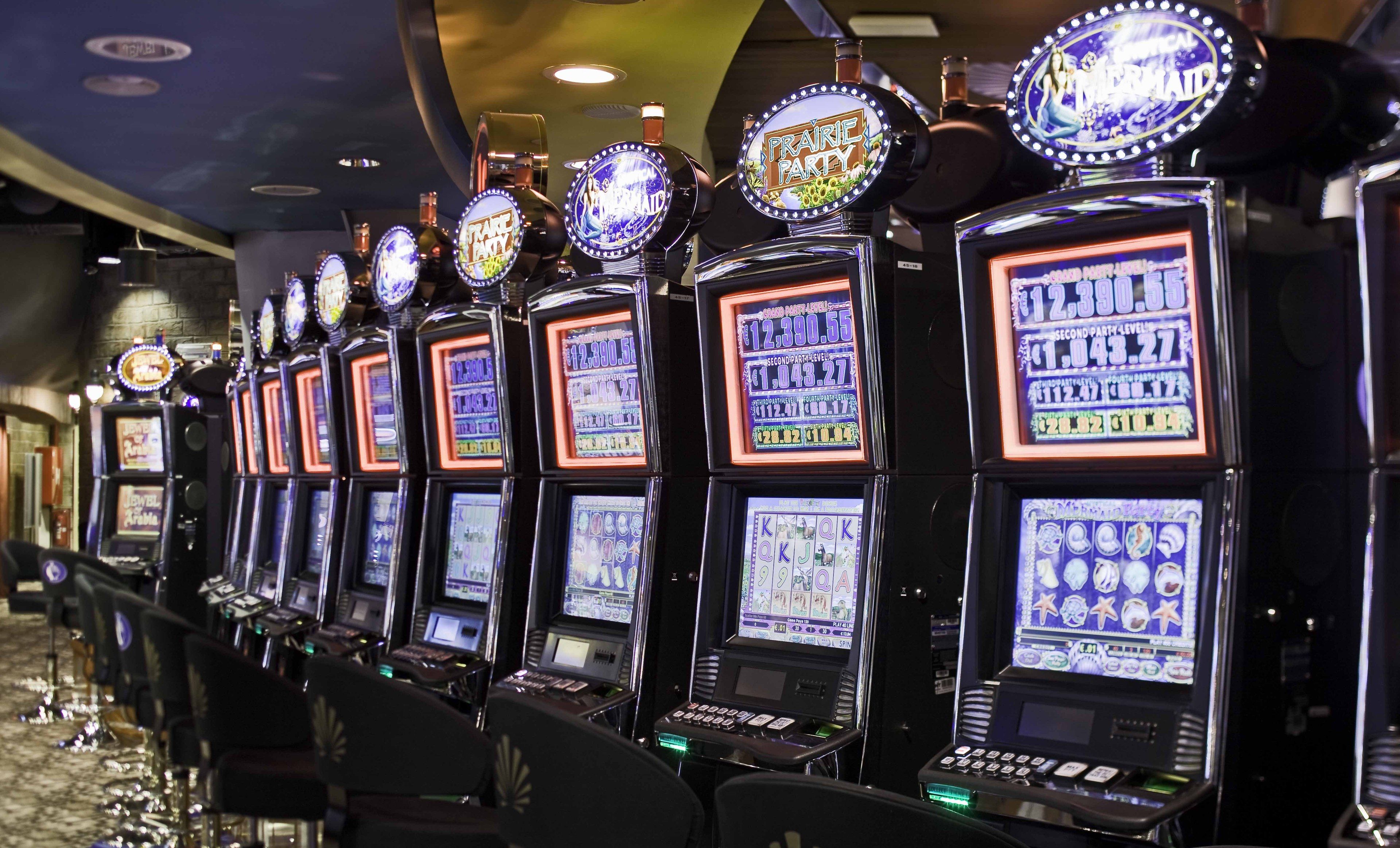A row of slot machines with illuminated screens and various game themes.