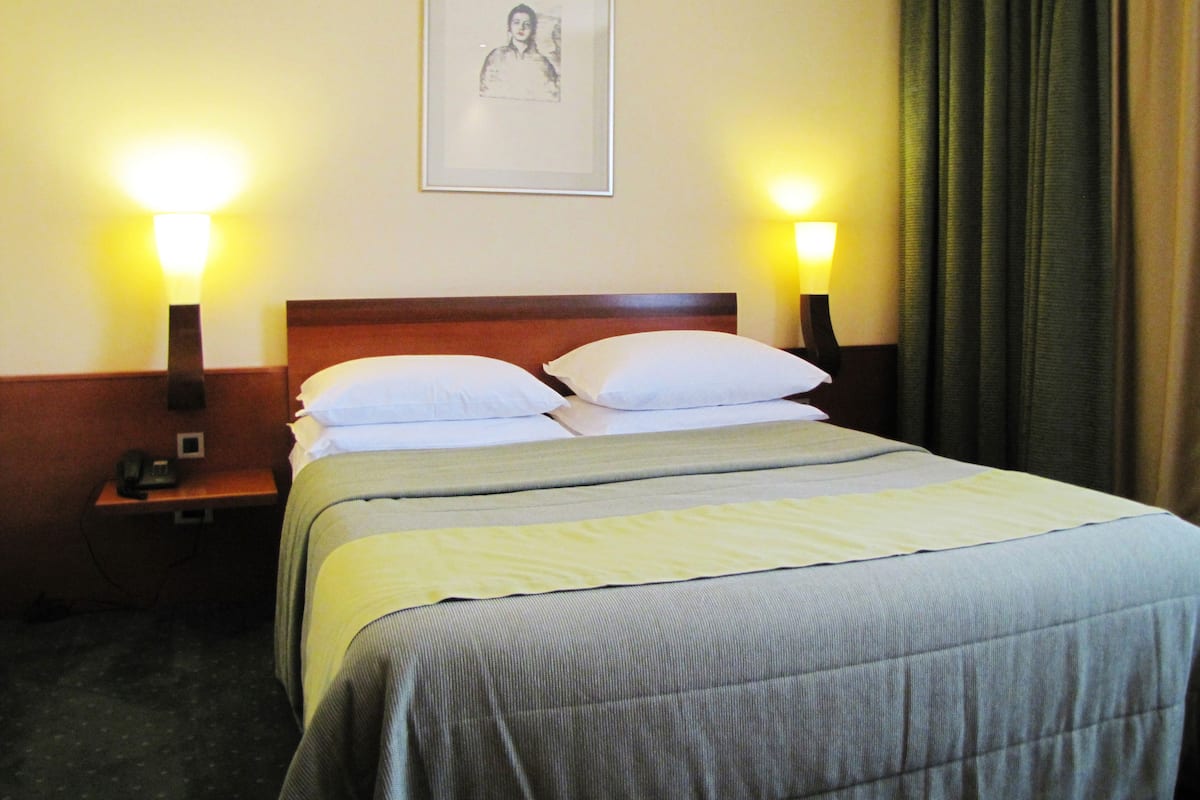 A hotel room with a bed, two bedside tables, a framed picture on the wall, and a curtain.