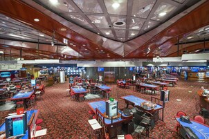 A casino with multiple gaming tables and slot machines, carpeted floors, and wooden ceiling panels.