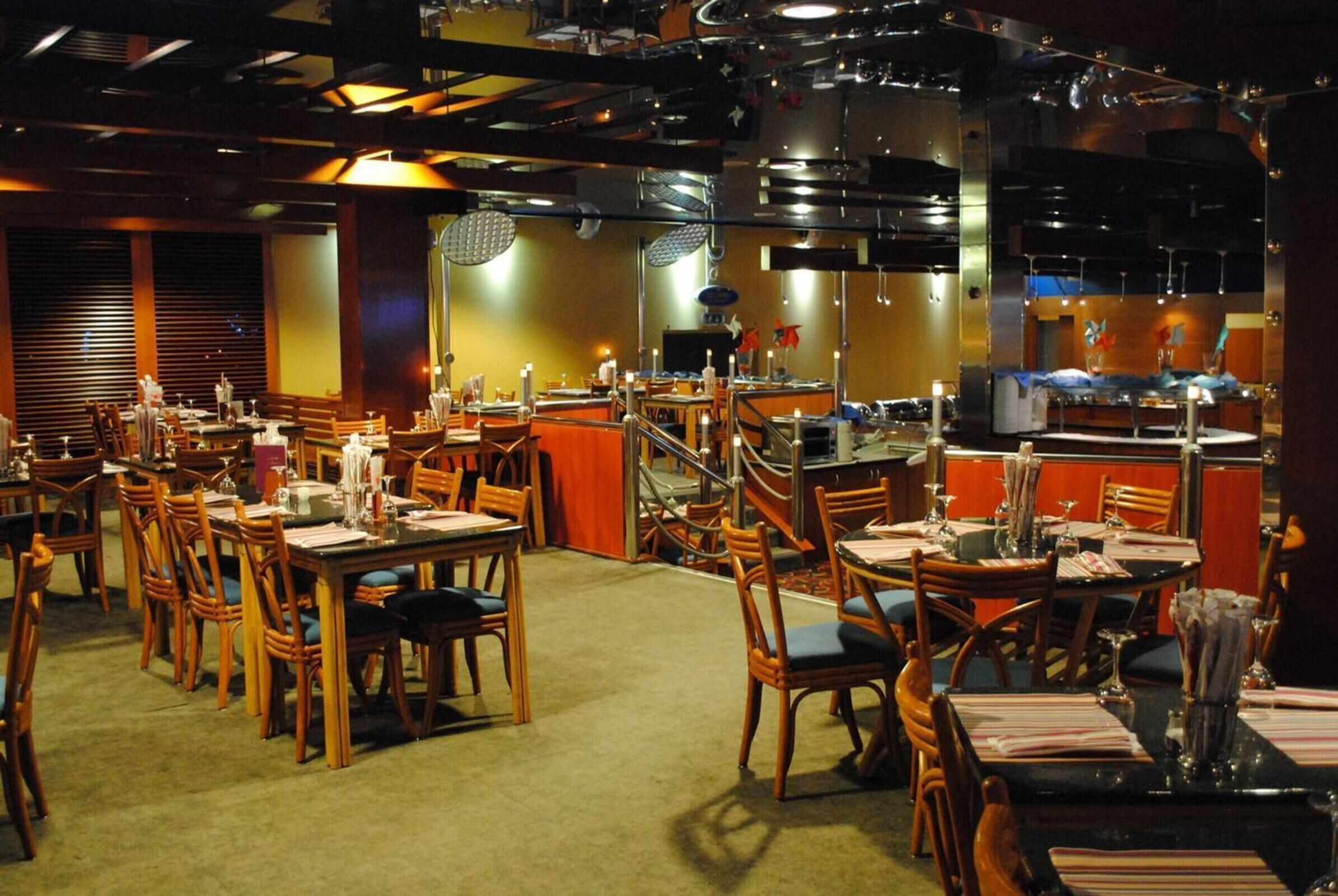 A restaurant with multiple dining tables and chairs, a bar area, and a kitchen visible in the background.