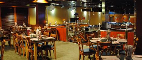A restaurant with multiple dining tables and chairs, a bar area, and a kitchen visible in the background.