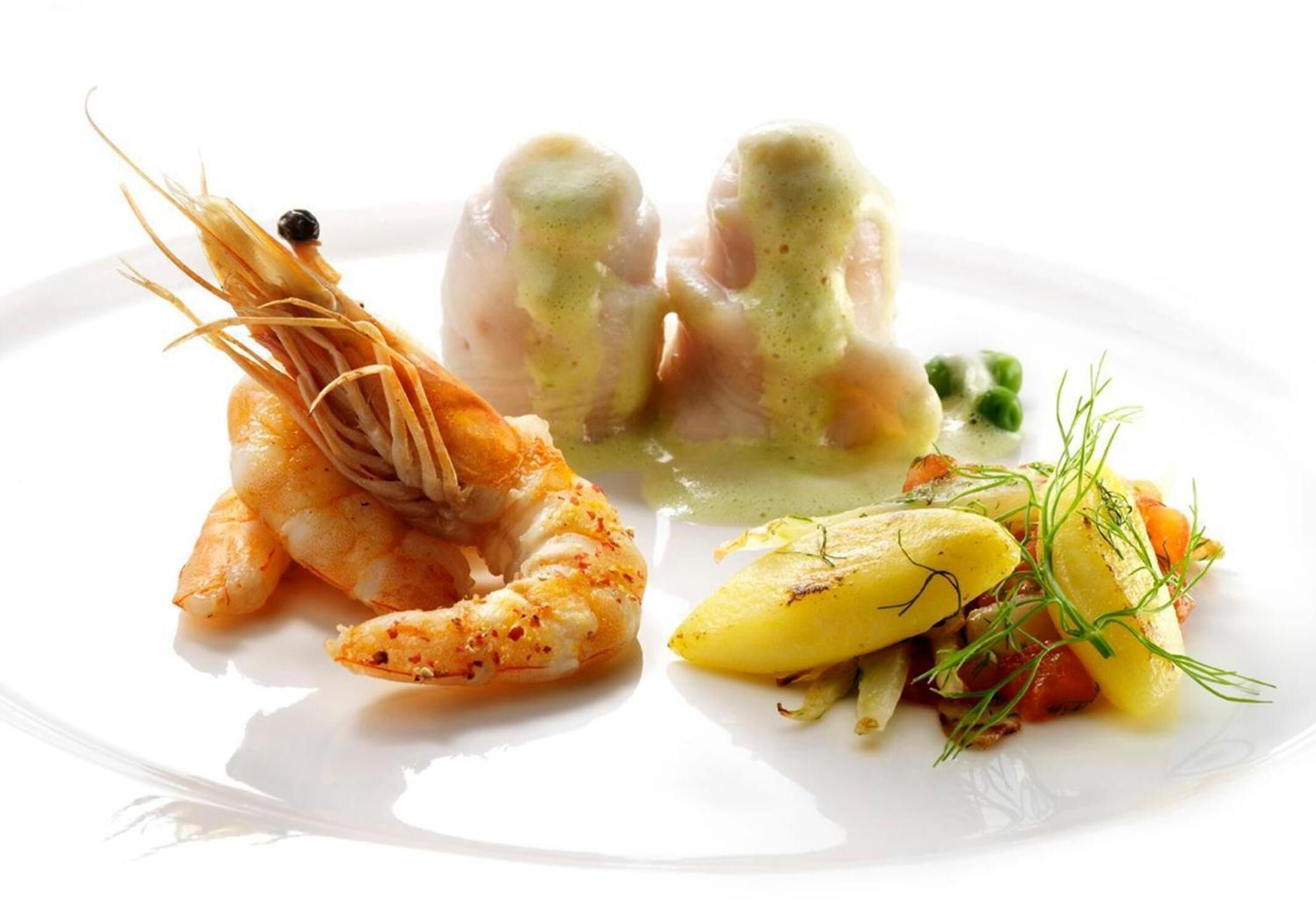 A plate with shrimp, a green sauce, and a side of potatoes and greens.