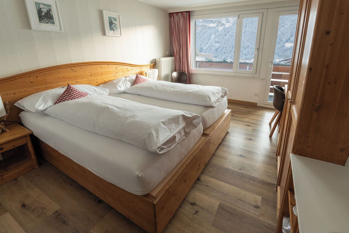 Una cama doble con ropa de cama blanca, un cabecero de madera y vistas a un paisaje nevado por la ventana.
