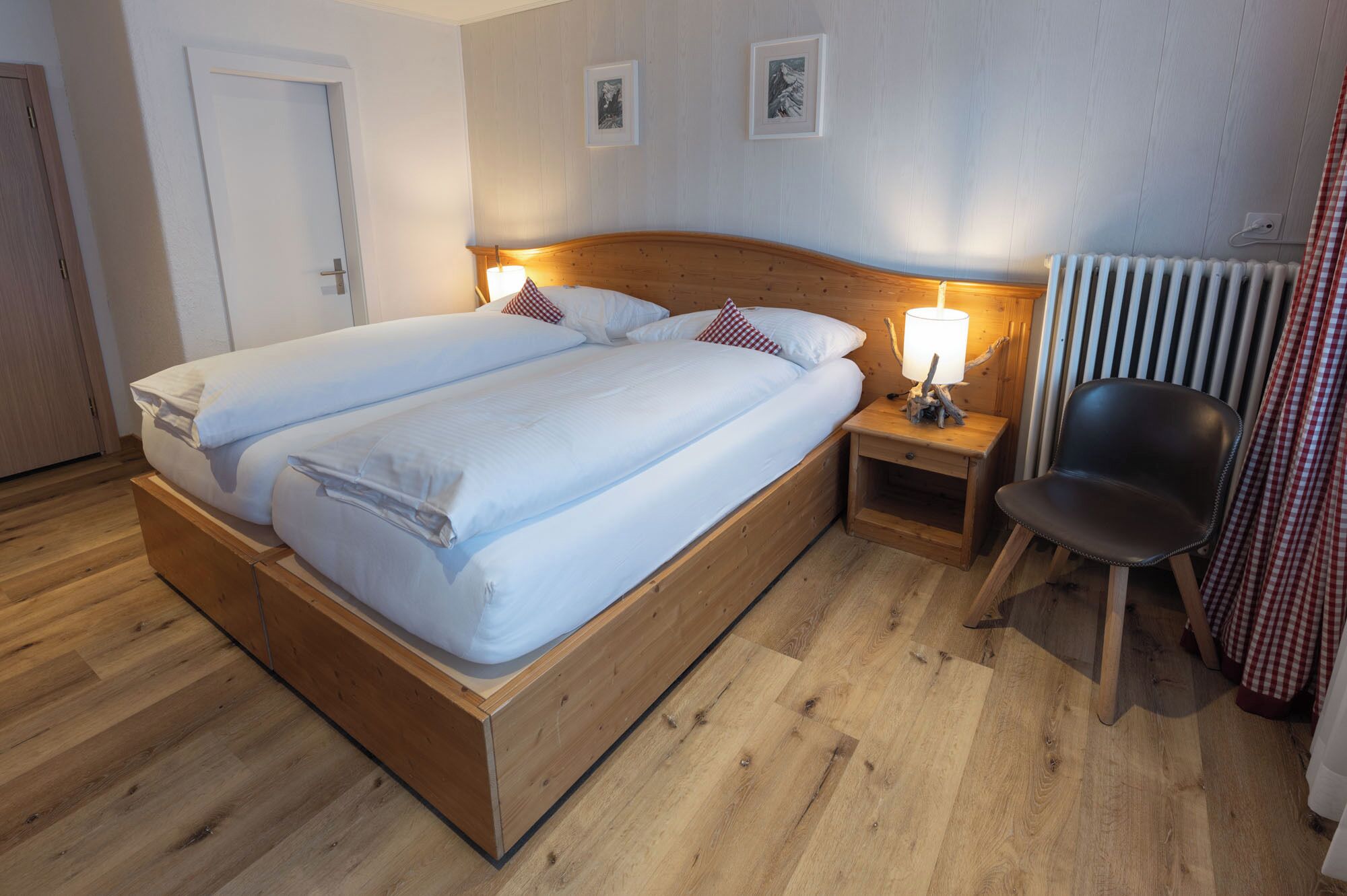 Ein Doppelbett mit weißen Leinen, zwei Nachttische mit Lampen, ein schwarzer Stuhl und eine Heizung.