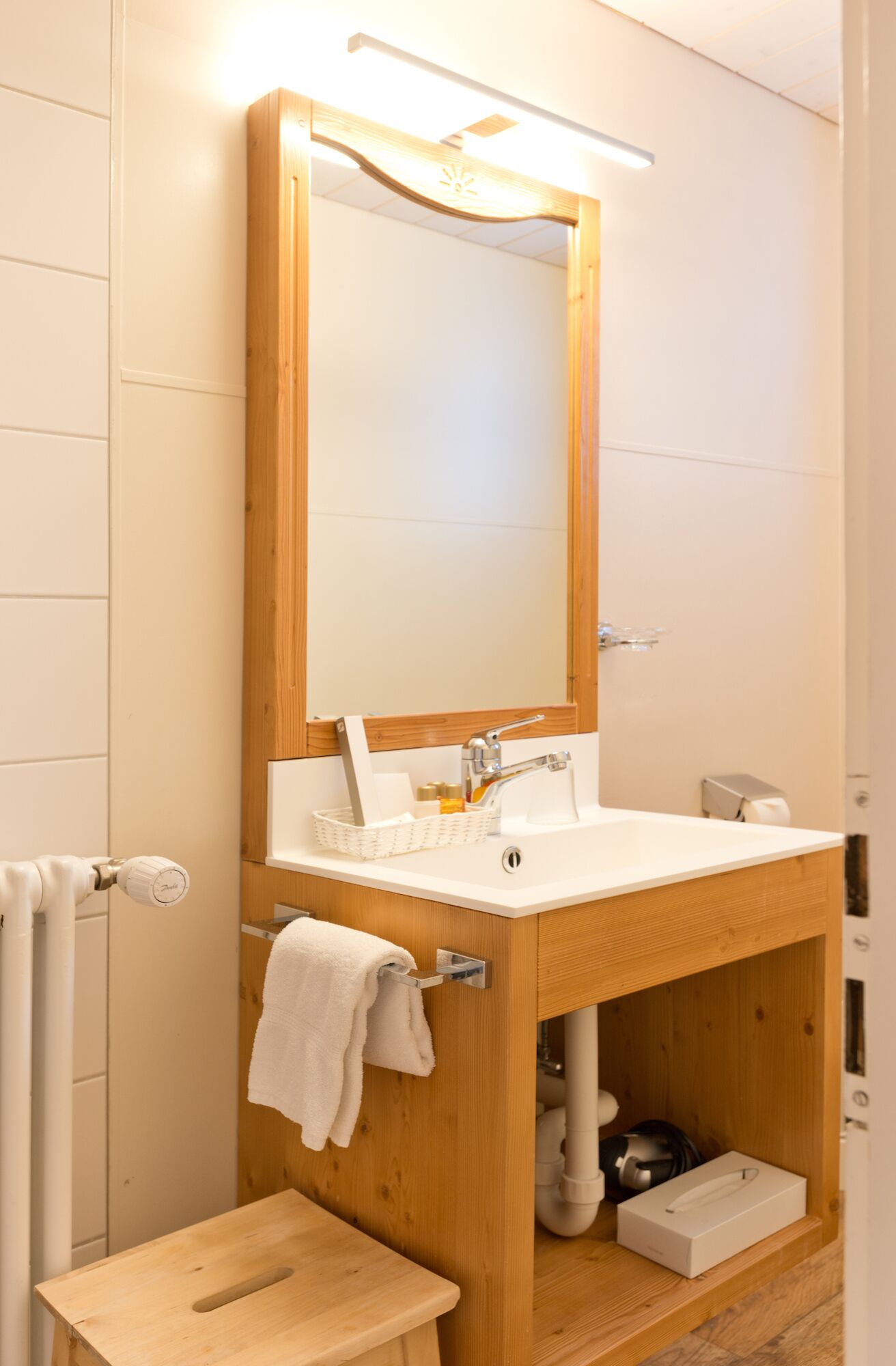 A compact bathroom with a wooden vanity, a white sink, and a mirror.