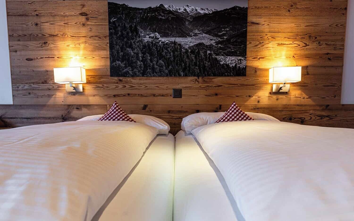 Une chambre avec un grand lit, des murs lambrissés en bois, deux lampes de chevet et un tableau représentant un paysage de montagne.