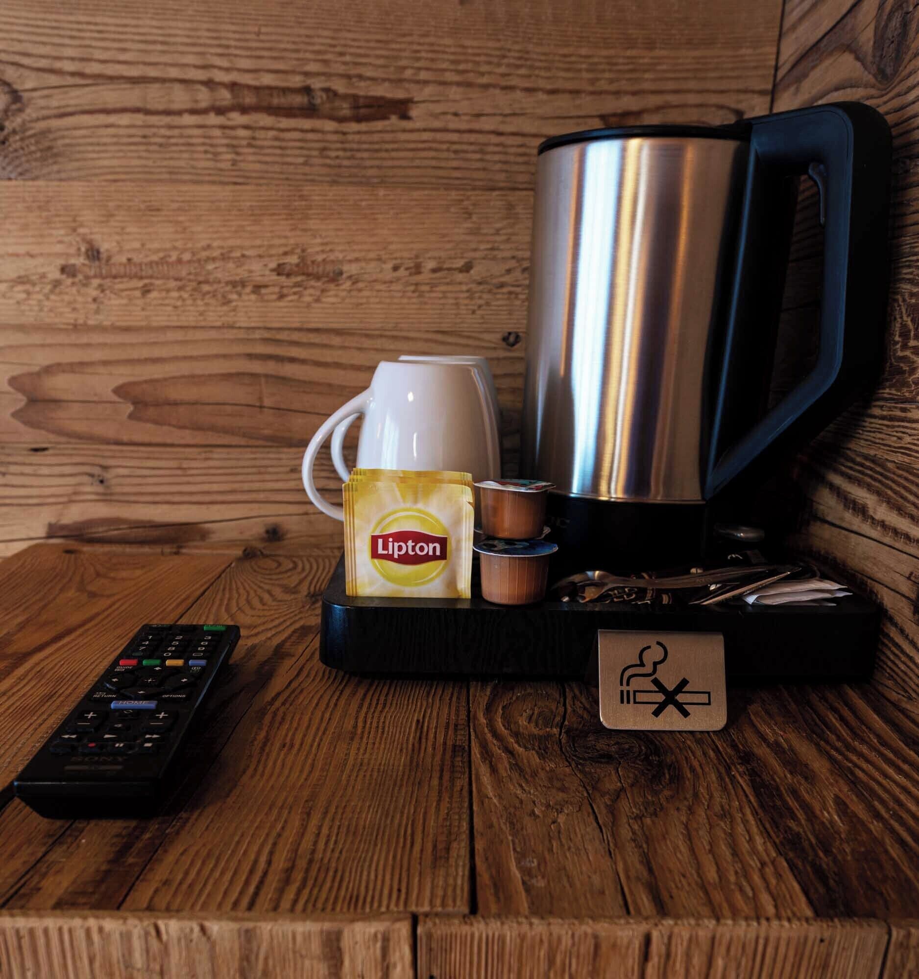 A coffee maker, Lipton tea bag, and a remote control on a wooden table.