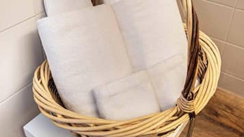 Un panier en osier contenant des serviettes blanches, posé sur une table blanche dans une salle de bain.