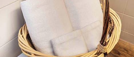 Una cesta de mimbre con toallas blancas sobre una mesa blanca en un baño.