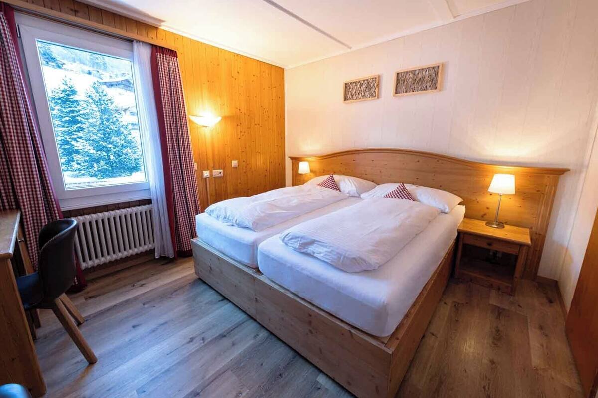 Una cama doble con dos mesitas de noche, una silla y una ventana con cortinas.