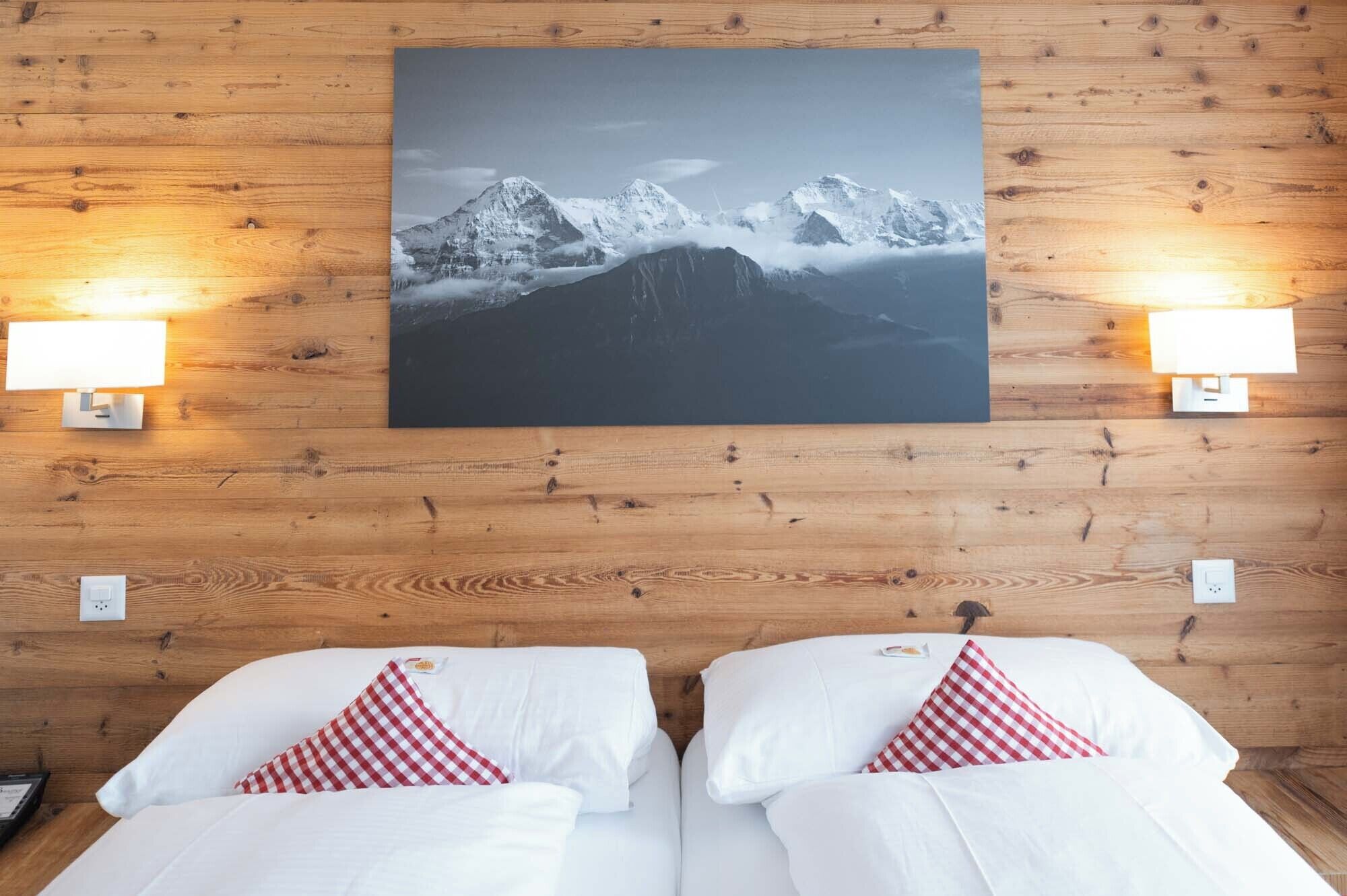 Ein Hotelzimmer mit zwei Betten, einem großen Berglandschaftsbild darüber und zwei Wandlampen.