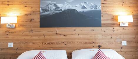 Ein Hotelzimmer mit zwei Betten, einem großen Berglandschaftsbild darüber und zwei Wandlampen.